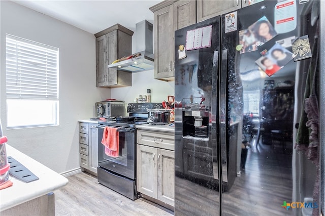 kitchen with light hardwood / wood-style floors, wall chimney range hood, and black appliances