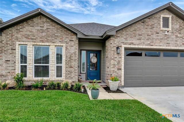 213 Flint Rock Ct, Victoria, TX 77904 - view of front of house with a front yard, concrete driveway, brick siding, an attached garage, and a shingled roof