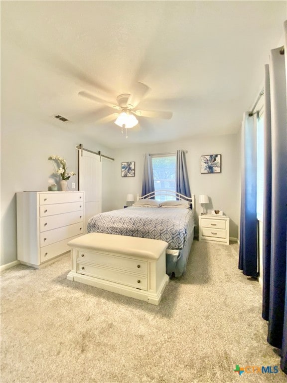 carpeted bedroom with a barn door and ceiling fan