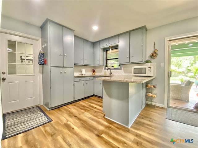 kitchen featuring a kitchen breakfast bar, light hardwood / wood-style floors, kitchen peninsula, and gray cabinets