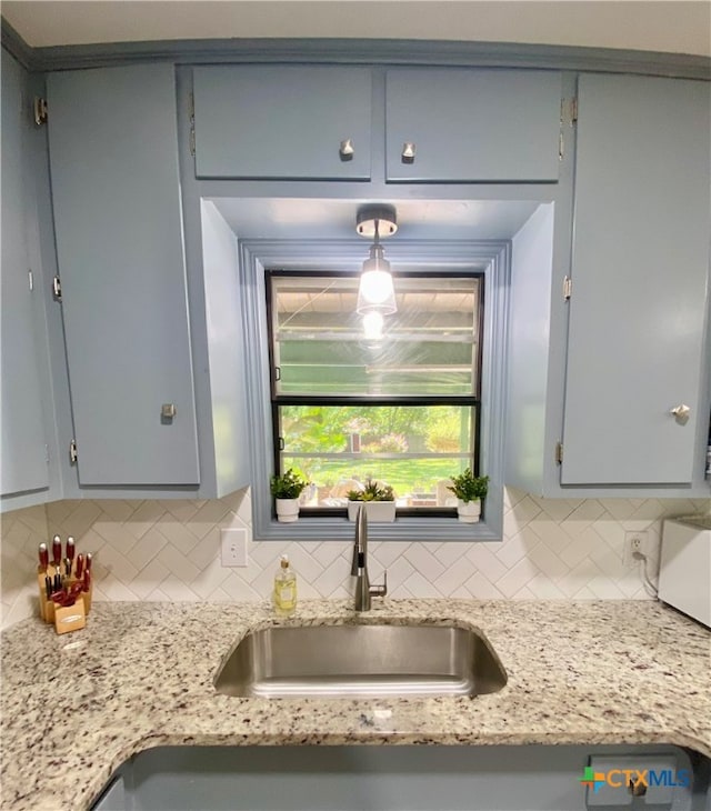 kitchen featuring gray cabinetry, sink, light stone counters, and backsplash