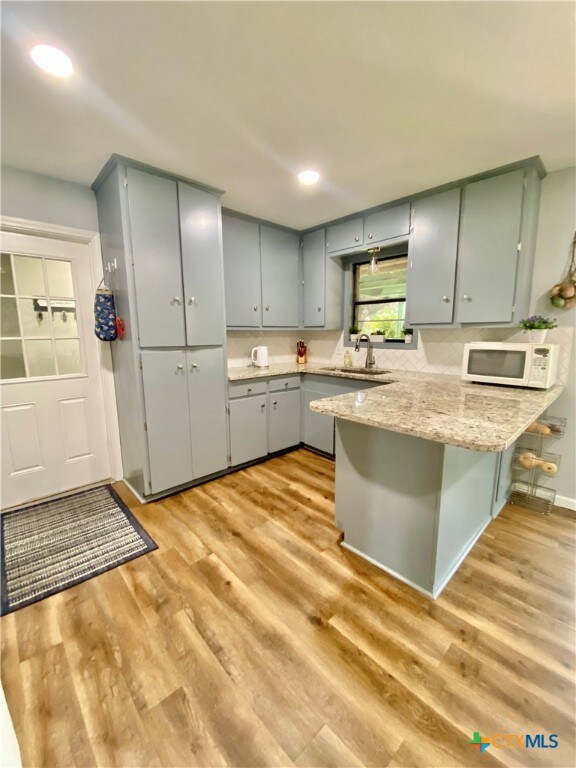 kitchen with kitchen peninsula, light hardwood / wood-style flooring, sink, and a breakfast bar