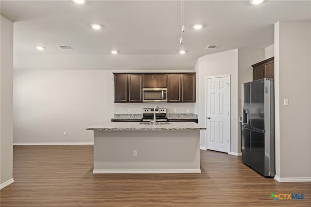 kitchen featuring dark hardwood / wood-style flooring, stainless steel appliances, light stone counters, and an island with sink