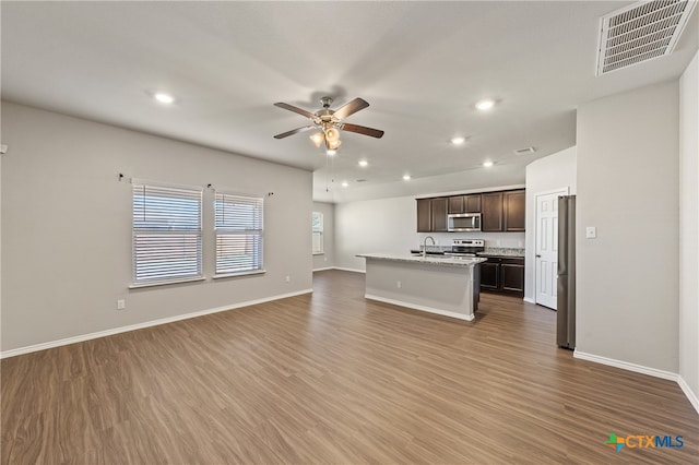 kitchen featuring appliances with stainless steel finishes, hardwood / wood-style flooring, dark brown cabinets, and an island with sink