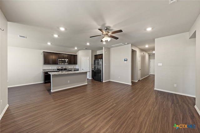 kitchen with appliances with stainless steel finishes, dark brown cabinetry, ceiling fan, a center island with sink, and dark hardwood / wood-style floors