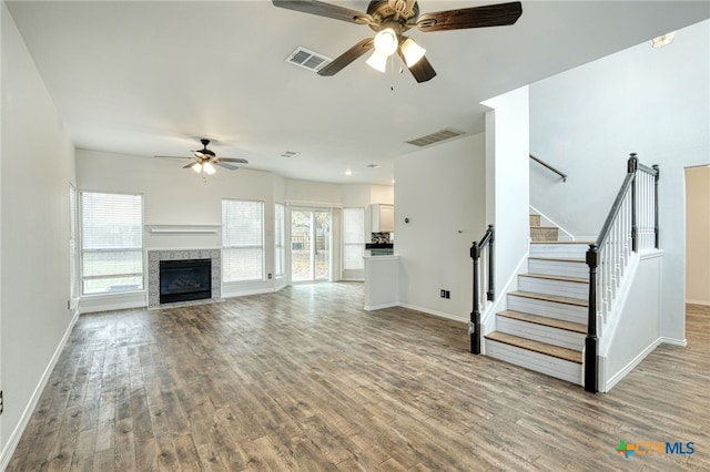 unfurnished living room with a tiled fireplace, ceiling fan, and light hardwood / wood-style floors