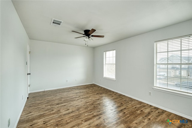 empty room featuring ceiling fan, a healthy amount of sunlight, and dark wood-type flooring