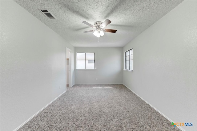 spare room with visible vents, baseboards, light colored carpet, a textured ceiling, and a ceiling fan