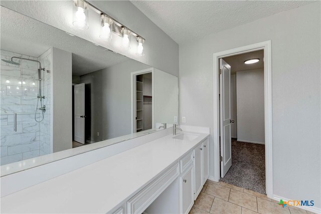 bathroom featuring vanity, baseboards, a tile shower, a textured ceiling, and tile patterned floors