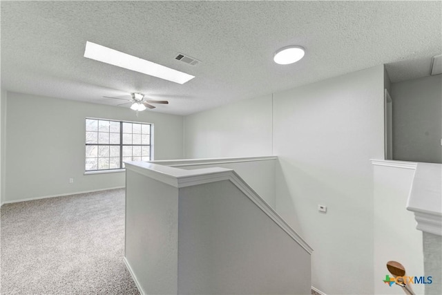 hallway with visible vents, baseboards, carpet, an upstairs landing, and a skylight