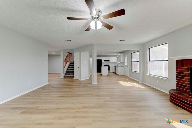 unfurnished living room featuring light wood-style flooring, a textured ceiling, stairway, a fireplace, and baseboards