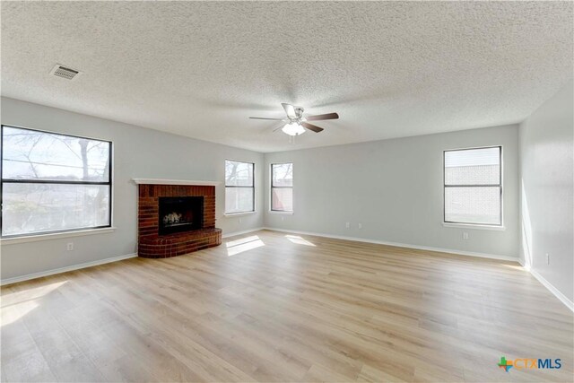 unfurnished living room with visible vents, a brick fireplace, baseboards, light wood-style flooring, and a ceiling fan