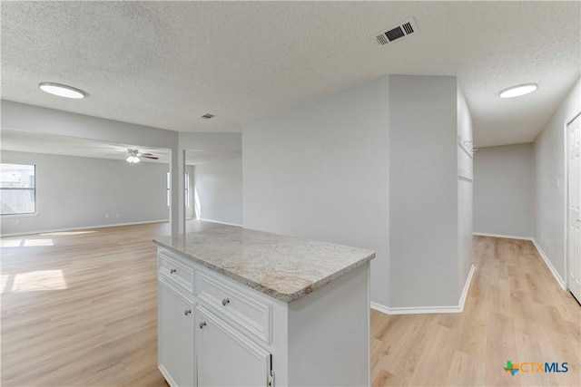 kitchen with visible vents, white cabinetry, light wood-style floors, and light stone countertops