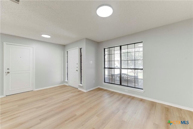 empty room featuring light wood-style flooring, baseboards, and a textured ceiling