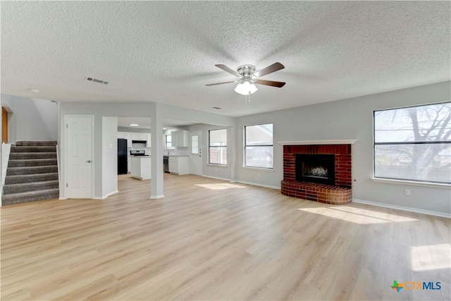 unfurnished living room featuring stairs, a fireplace, visible vents, and light wood finished floors