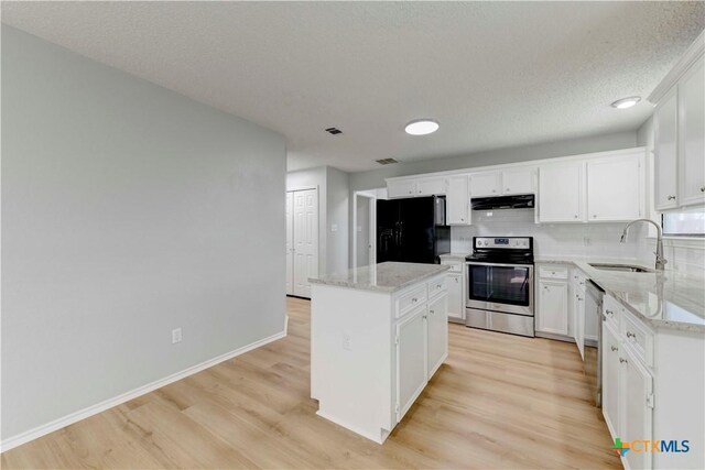 kitchen with a sink, under cabinet range hood, a center island, stainless steel appliances, and light wood-style floors