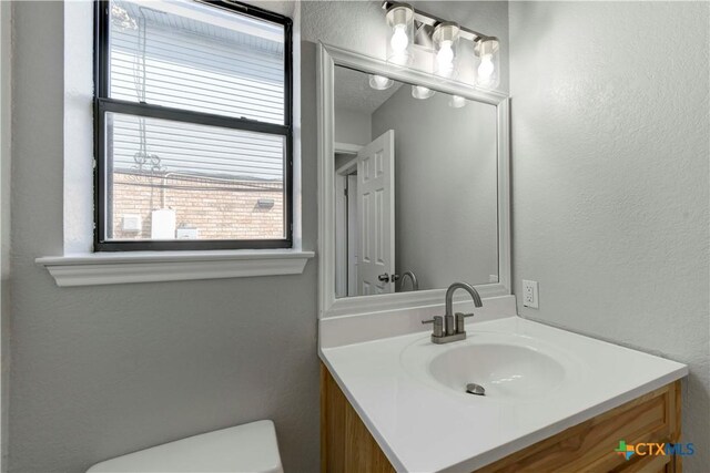 half bath featuring toilet, vanity, and a textured wall