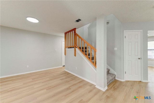 stairway featuring a textured ceiling, wood finished floors, visible vents, and baseboards