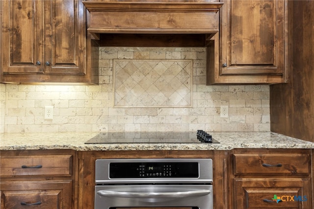 kitchen with light stone counters, oven, decorative backsplash, black electric stovetop, and custom exhaust hood