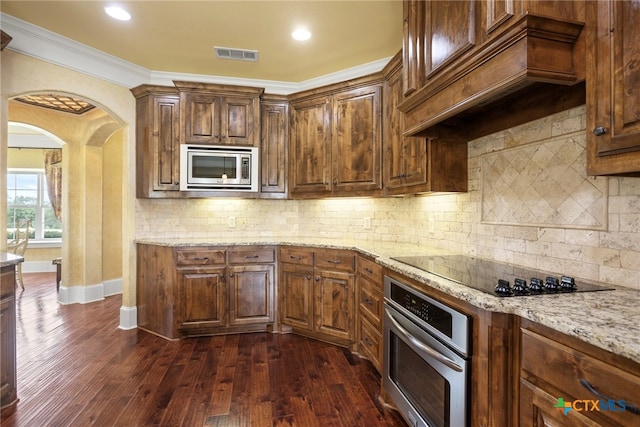 kitchen with dark wood-type flooring, crown molding, appliances with stainless steel finishes, light stone counters, and custom range hood