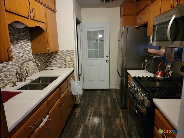 kitchen featuring stainless steel appliances, dark wood-style flooring, a sink, backsplash, and brown cabinets