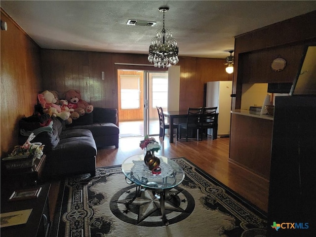 living room featuring visible vents, wood finished floors, a textured ceiling, wood walls, and a notable chandelier