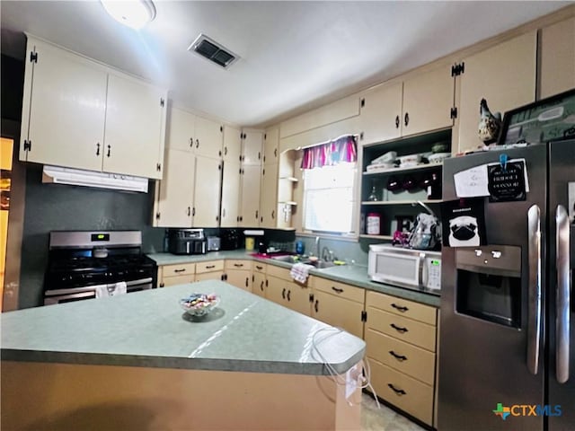 205 Coke St, Yoakum, TX 77995 - kitchen with appliances with stainless steel finishes, under cabinet range hood, open shelves, and cream cabinetry