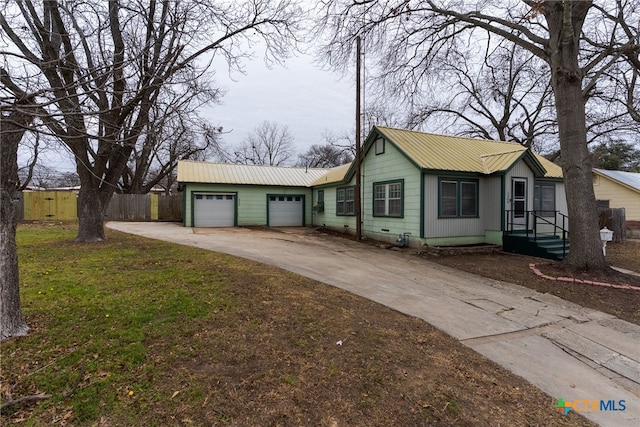 ranch-style home with metal roof, an attached garage, fence, driveway, and a front lawn