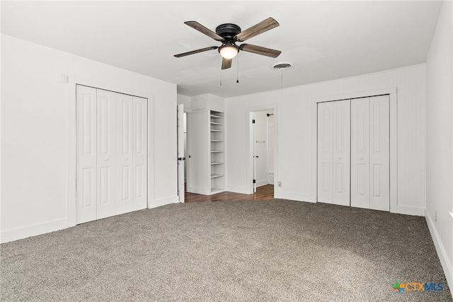 unfurnished bedroom featuring ceiling fan, carpet flooring, visible vents, baseboards, and multiple closets