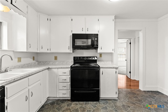 kitchen featuring a sink, white cabinets, light countertops, black appliances, and stone finish floor