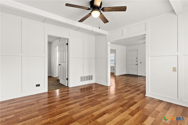 interior space with a ceiling fan, visible vents, a decorative wall, and wood finished floors