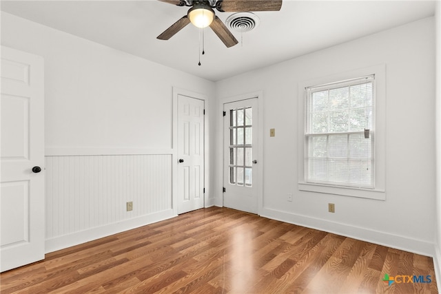 spare room featuring light wood-style floors, ceiling fan, baseboards, and a wainscoted wall