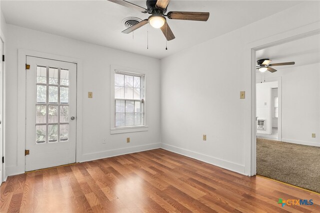 unfurnished room with a ceiling fan, visible vents, baseboards, and wood finished floors