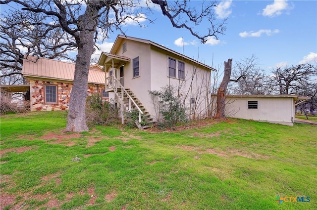 view of side of property featuring stairs, stone siding, a yard, and metal roof