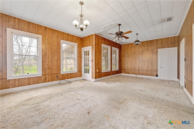 carpeted empty room featuring baseboards, wooden walls, visible vents, and ceiling fan with notable chandelier