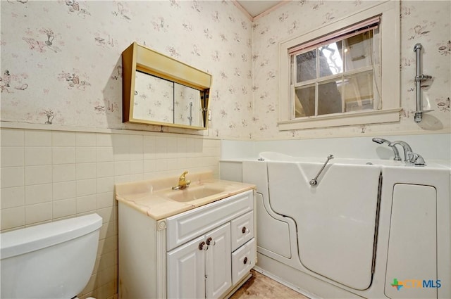 full bath with toilet, wallpapered walls, vanity, and wainscoting