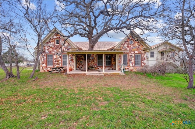 view of front of house with stone siding, metal roof, a front lawn, and a patio