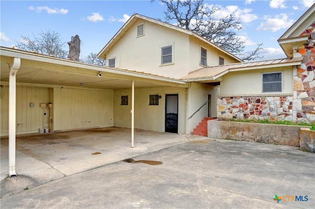 view of front facade with metal roof, driveway, an attached carport, and stucco siding