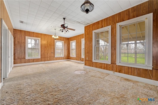 interior space with a ceiling fan, visible vents, plenty of natural light, and wooden walls