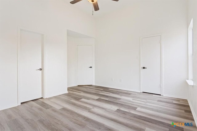 unfurnished bedroom featuring ceiling fan, a towering ceiling, and light hardwood / wood-style floors