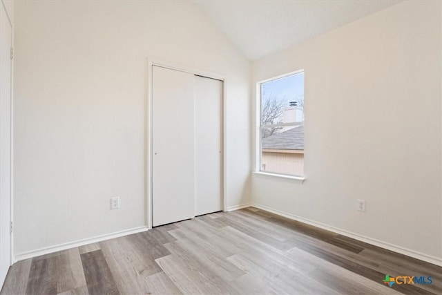 unfurnished bedroom with vaulted ceiling, a closet, and light hardwood / wood-style flooring