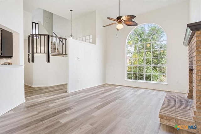 unfurnished living room featuring ceiling fan, a high ceiling, and light hardwood / wood-style flooring