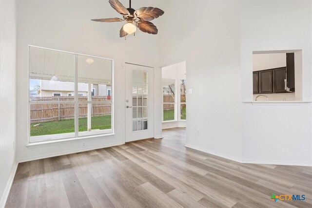 unfurnished living room featuring a high ceiling, light wood-type flooring, and ceiling fan