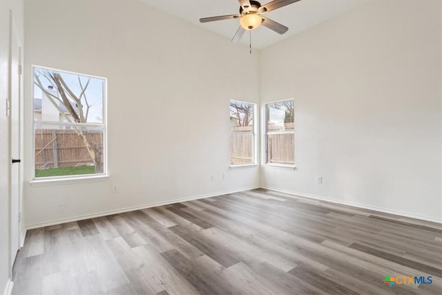 spare room featuring wood-type flooring, a towering ceiling, plenty of natural light, and ceiling fan