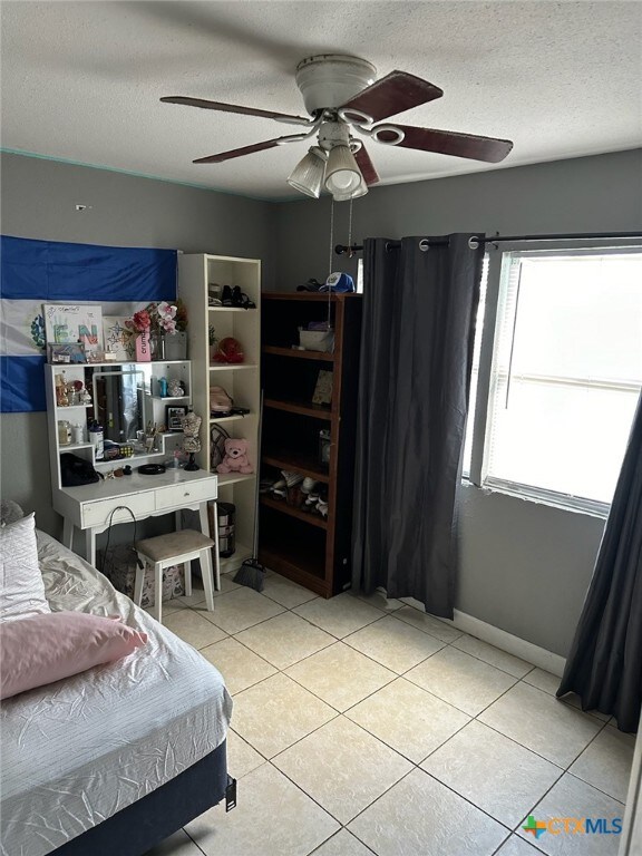 bedroom featuring a textured ceiling, light tile patterned floors, and ceiling fan