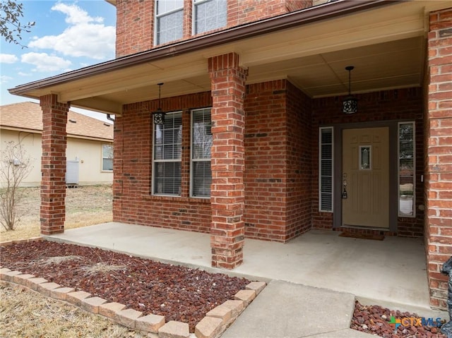 doorway to property featuring covered porch and brick siding