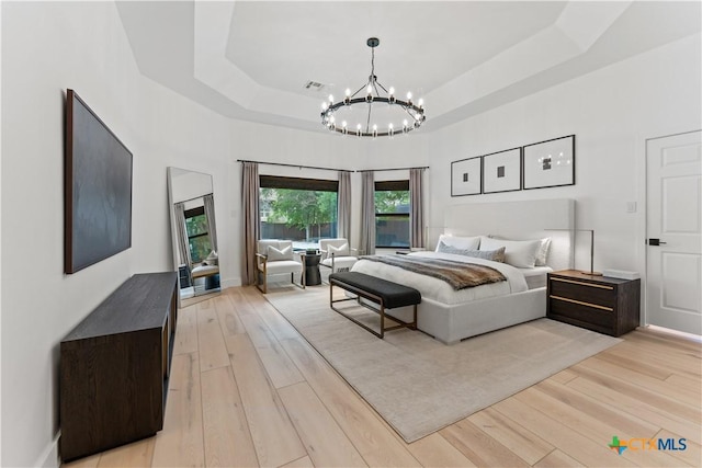 bedroom with an inviting chandelier, light wood-type flooring, and a tray ceiling