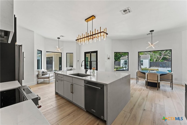 kitchen with sink, hanging light fixtures, gray cabinets, a kitchen island with sink, and light wood-type flooring