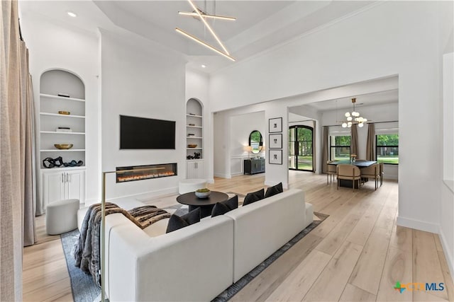 living room with light hardwood / wood-style floors, built in features, a high ceiling, and a chandelier