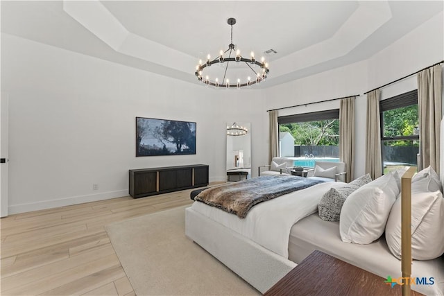 bedroom featuring a notable chandelier, light hardwood / wood-style floors, and a raised ceiling